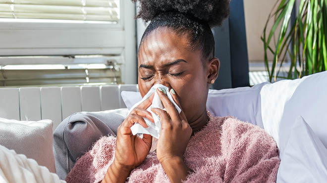 Person holding a tissue to their face, experiencing a blocked nose for a month with clear mucus
